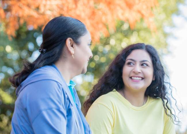 Mature woman mentoring Indian teenage girl outdoors on park bench